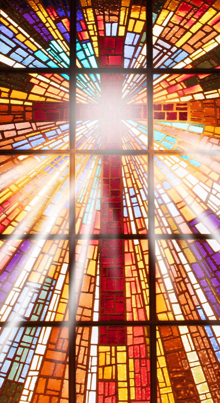 Sun rays coming from the center of a stained glass window with a cross.